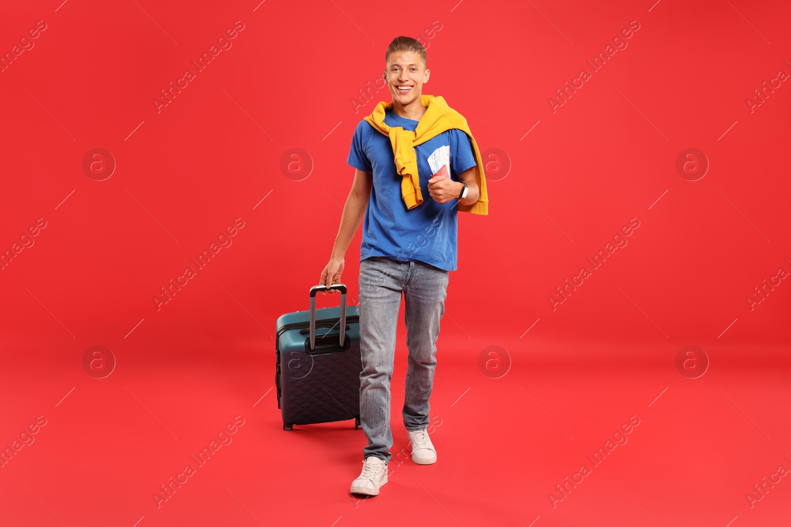 Photo of Happy traveller with suitcase, passport and tickets on red background