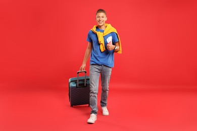 Photo of Happy traveller with suitcase, passport and tickets on red background