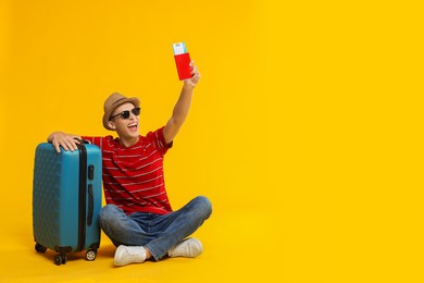 Happy traveller with suitcase, passport and ticket on yellow background, space for text