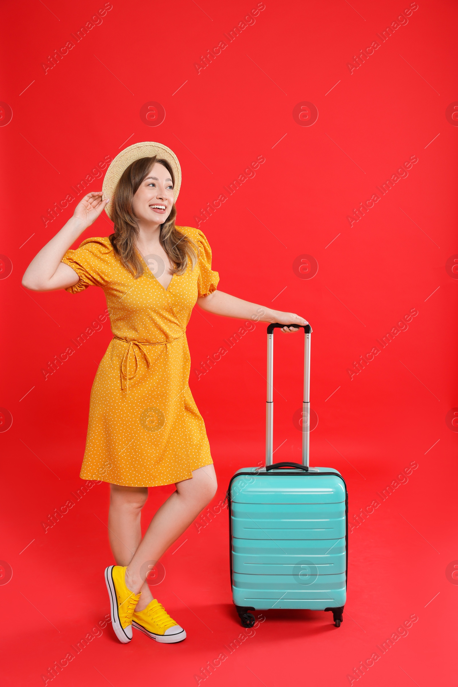 Photo of Happy traveller with suitcase on red background