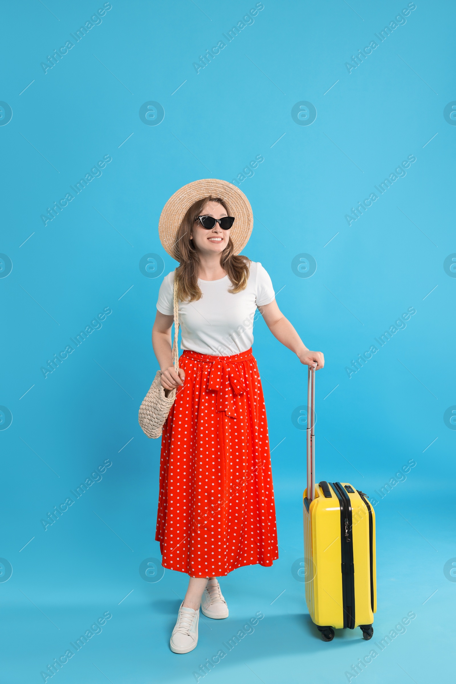 Photo of Happy traveller in sunglasses with suitcase on light blue background