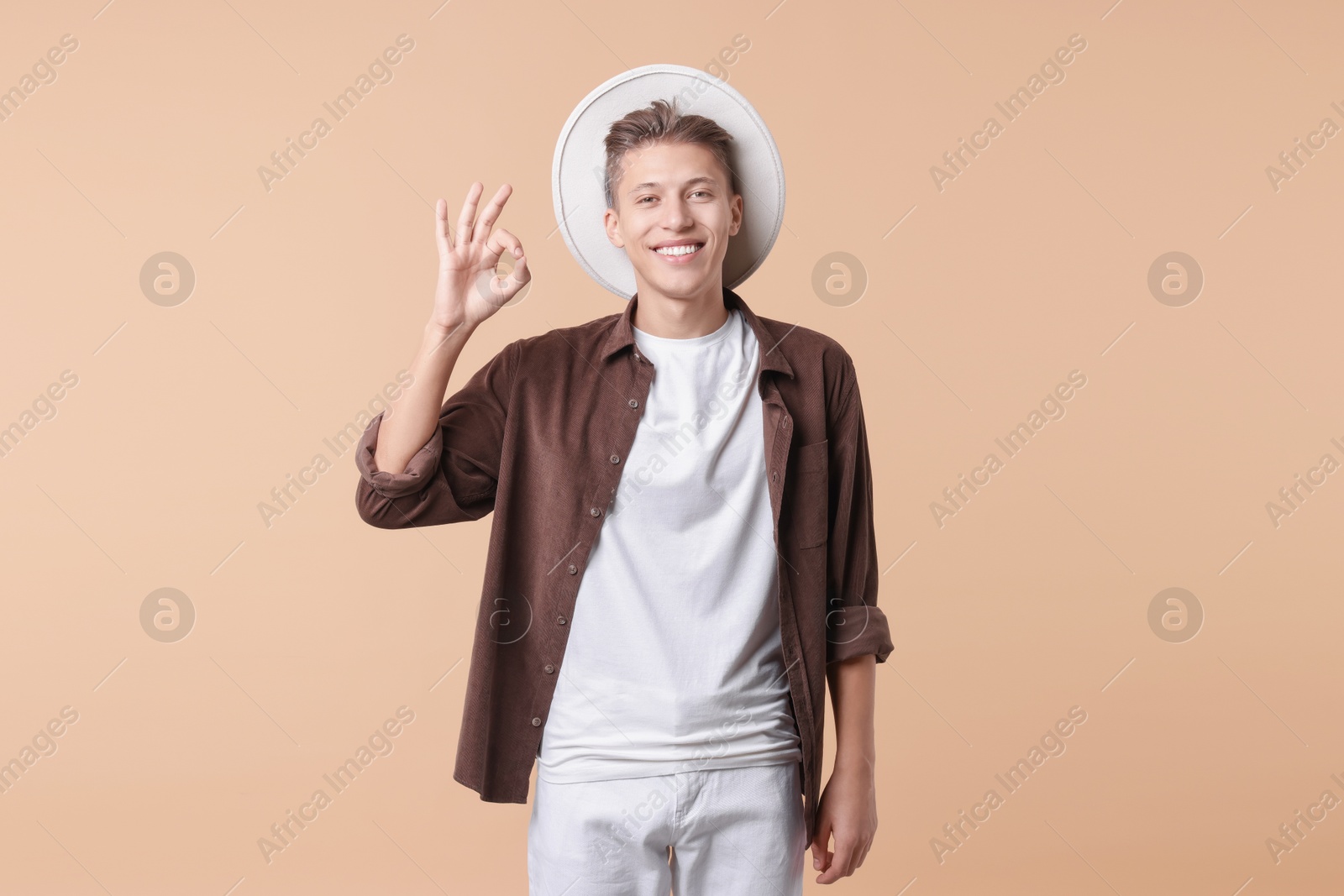 Photo of Happy young man showing OK gesture on beige background