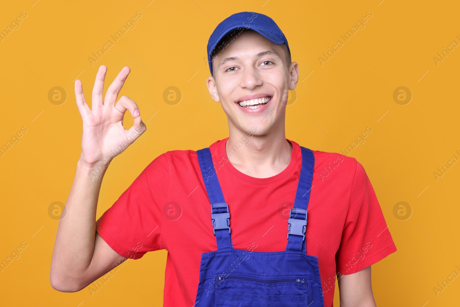 Photo of Happy young man in uniform showing OK gesture on orange background