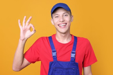 Happy young man in uniform showing OK gesture on orange background