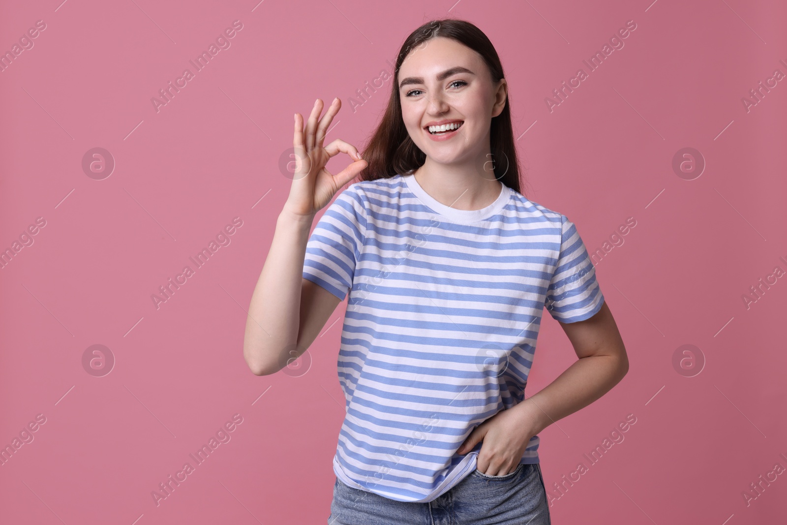 Photo of Happy young woman showing OK gesture on pink background