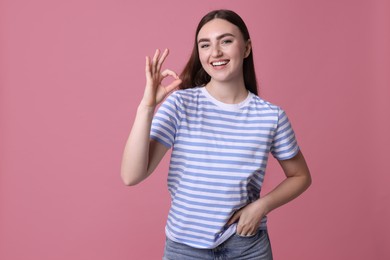 Happy young woman showing OK gesture on pink background