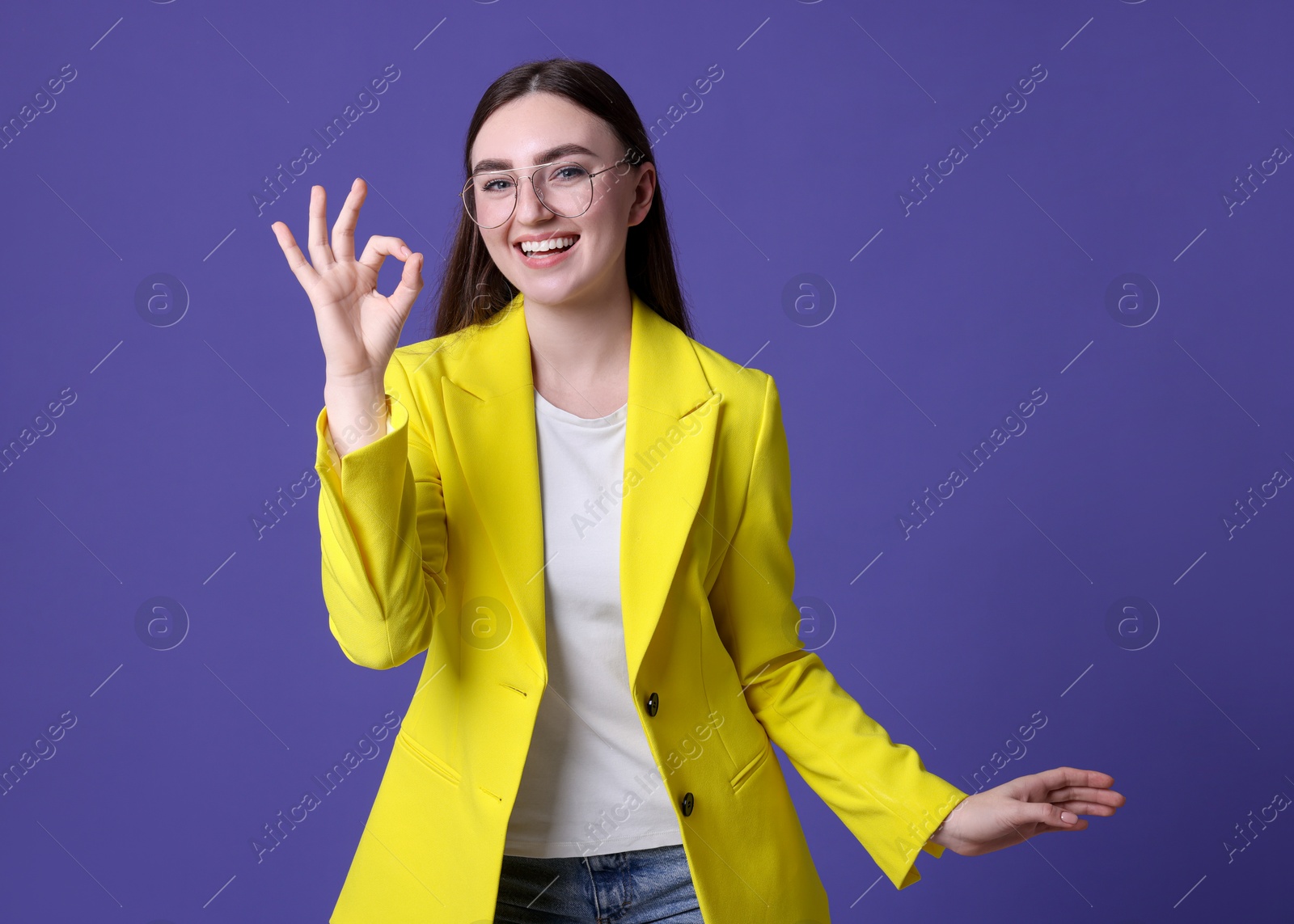 Photo of Happy young woman showing OK gesture on violet background