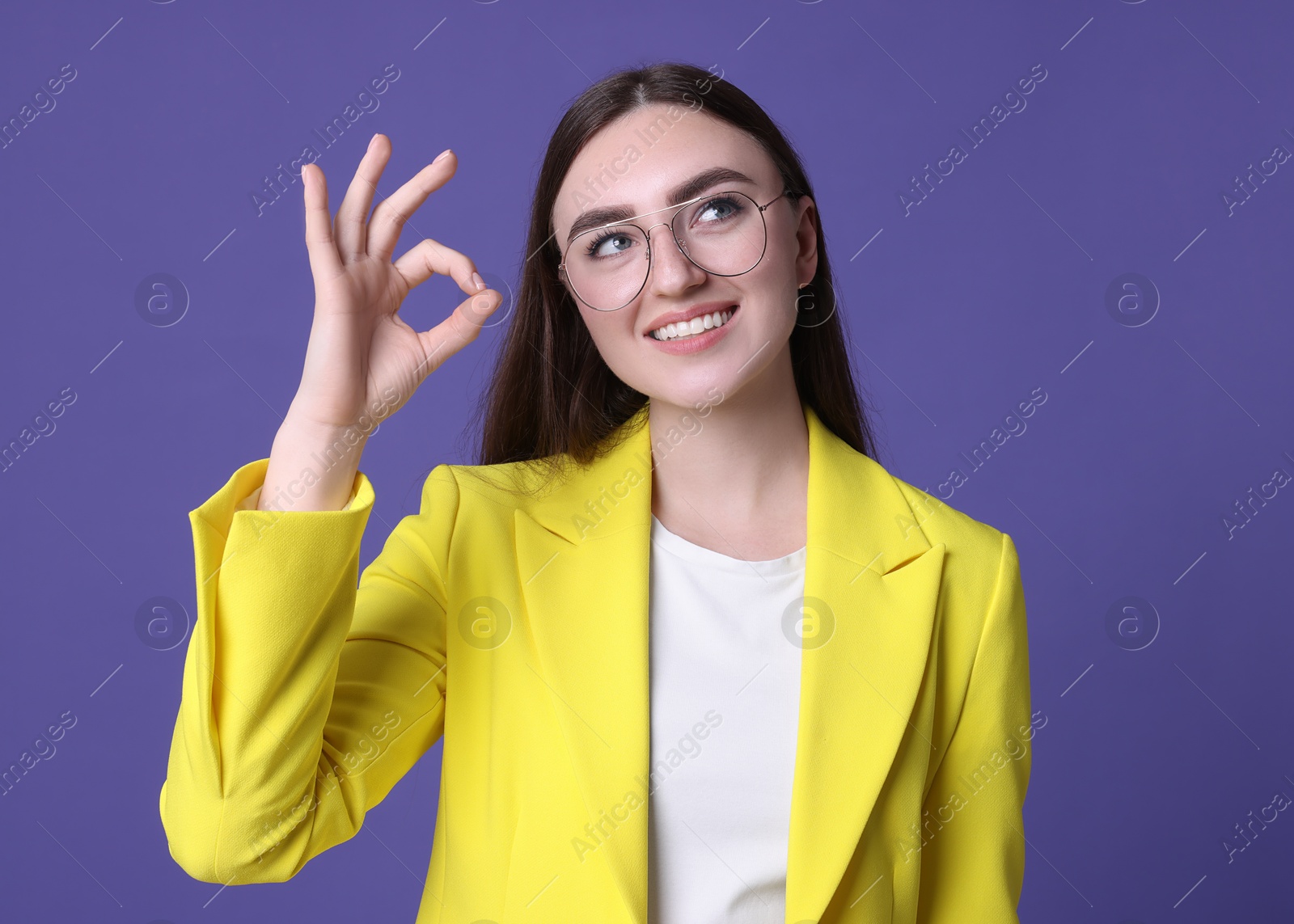 Photo of Happy young woman showing OK gesture on violet background