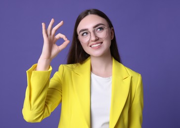 Happy young woman showing OK gesture on violet background