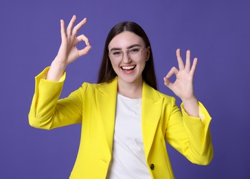 Photo of Happy young woman showing OK gesture on violet background