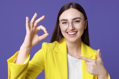 Photo of Happy young woman showing OK gesture on violet background