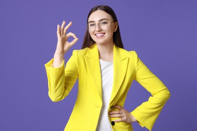 Photo of Happy young woman showing OK gesture on violet background