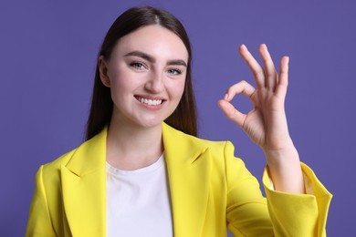 Happy young woman showing OK gesture on violet background