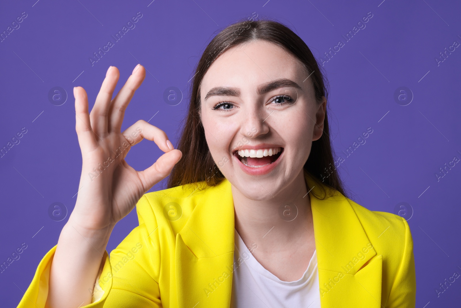 Photo of Happy young woman showing OK gesture on violet background