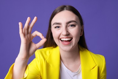 Photo of Happy young woman showing OK gesture on violet background