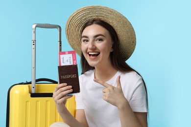 Woman with ticket, passport and suitcase on light blue background