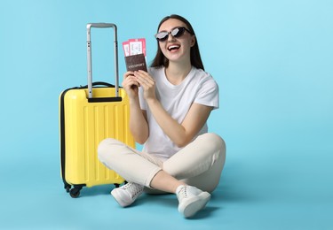 Woman with tickets, passport and suitcase on light blue background