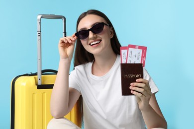 Photo of Woman with tickets, passport and suitcase on light blue background