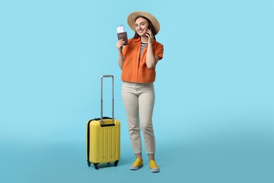 Photo of Woman with ticket, passport and suitcase talking on smartphone against light blue background