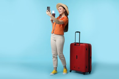 Photo of Woman with ticket, passport and suitcase taking selfie on light blue background