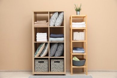 Photo of Home textile organization. Different pillows, linens towels and blankets on shelving units near beige wall