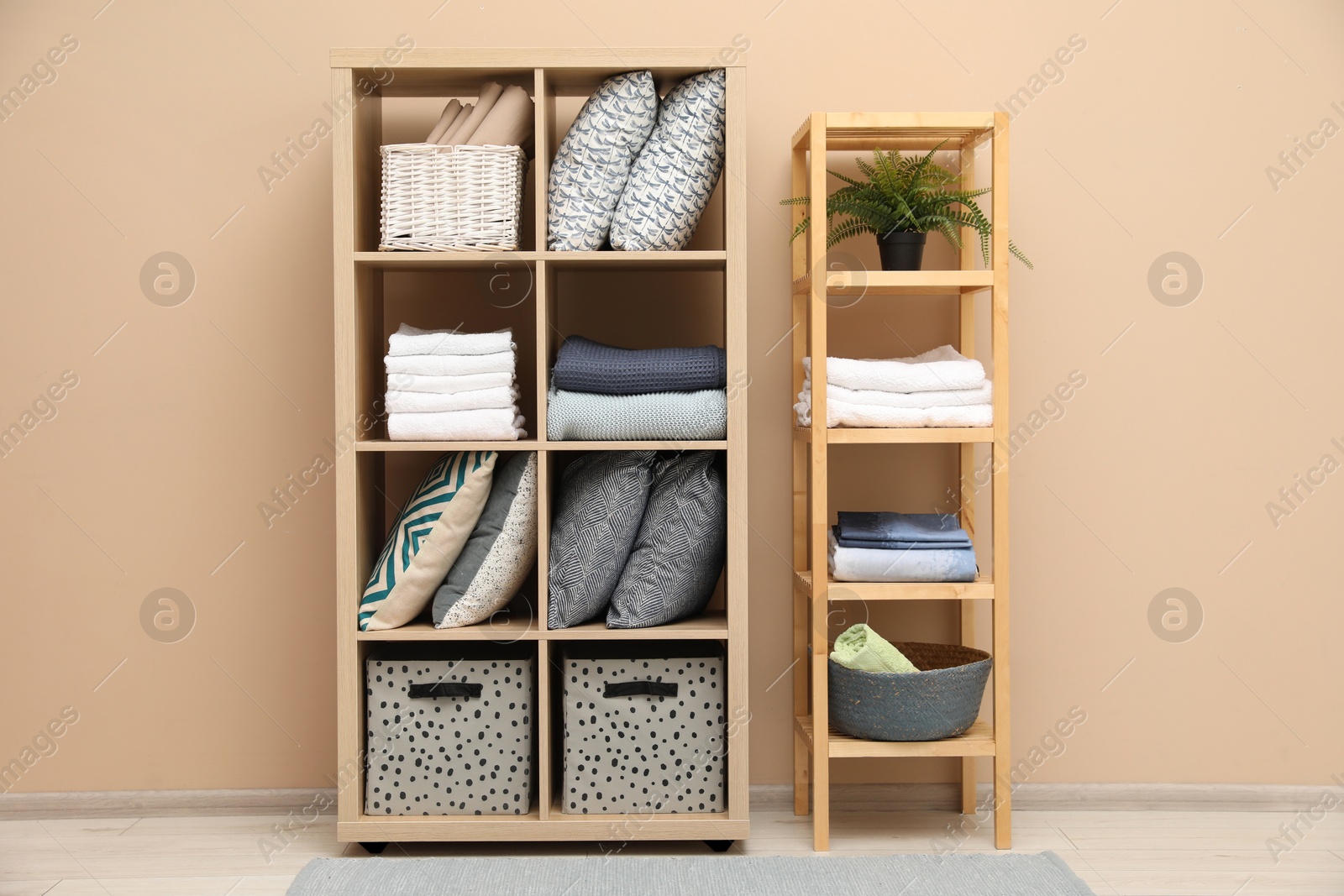 Photo of Home textile organization. Different pillows, linens towels and blankets on shelving units near beige wall