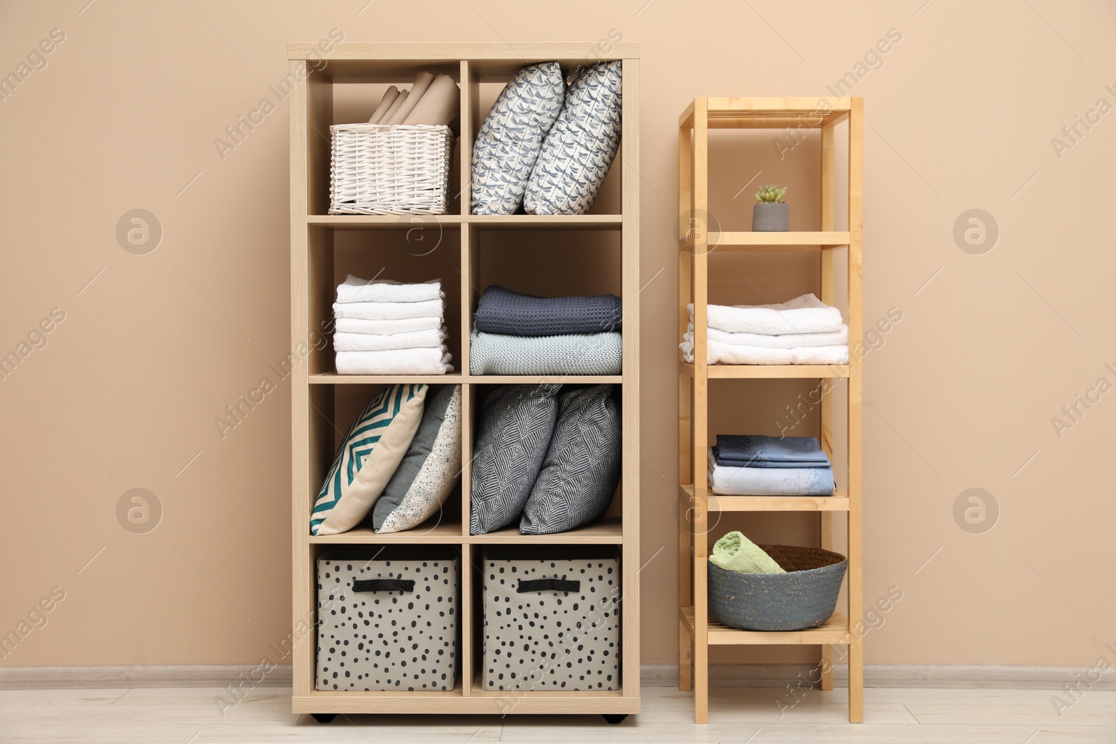 Photo of Home textile organization. Different pillows, linens and blankets on shelving units near beige wall