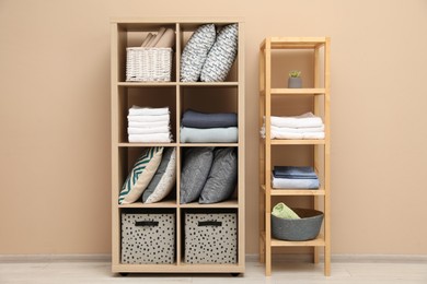 Home textile organization. Different pillows, linens and blankets on shelving units near beige wall