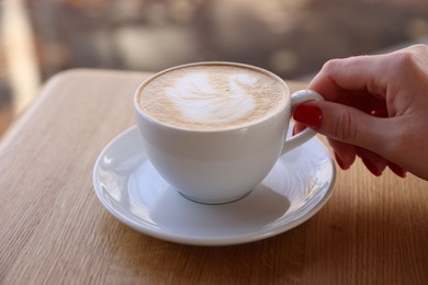 Photo of Woman with cup of aromatic coffee at wooden table in cafe, closeup