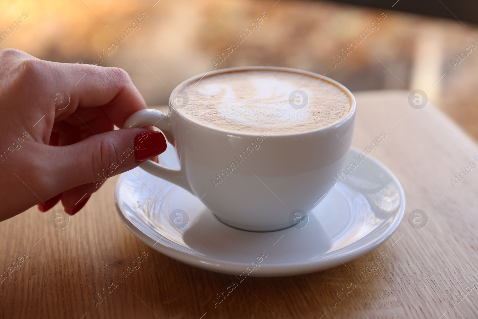 Photo of Woman with cup of aromatic coffee at wooden table in cafe, closeup