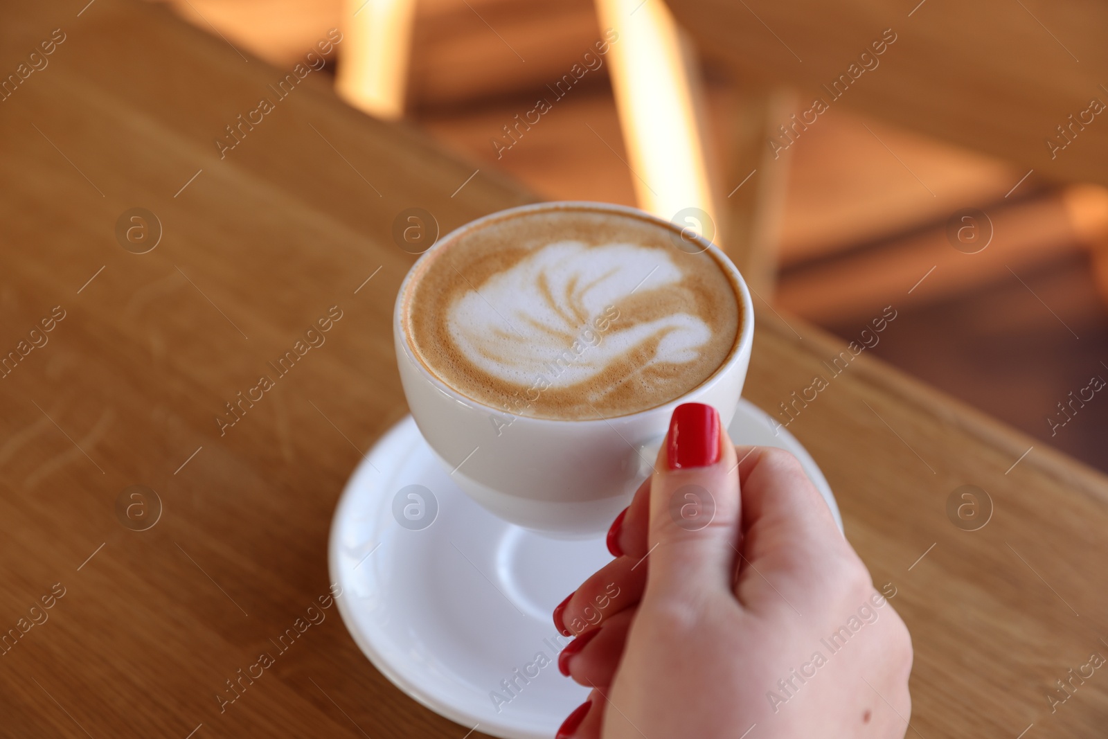 Photo of Woman with cup of aromatic coffee at wooden table in cafe, closeup