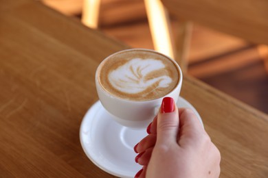 Photo of Woman with cup of aromatic coffee at wooden table in cafe, closeup