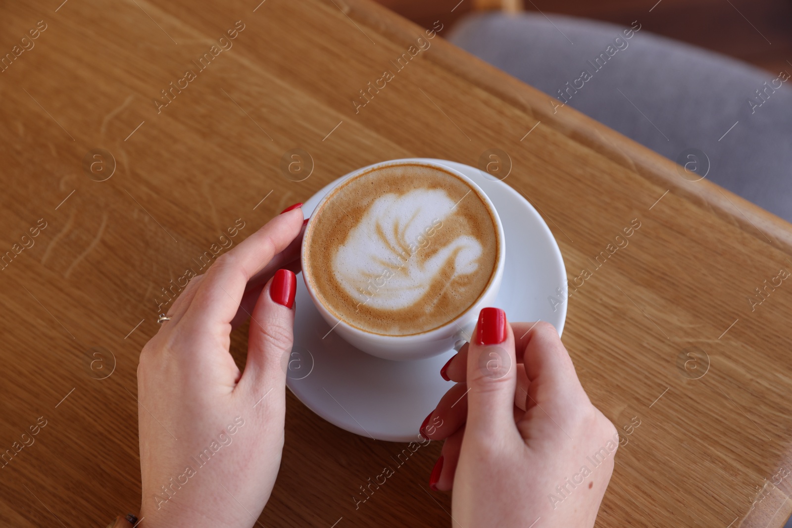 Photo of Woman with cup of aromatic coffee at wooden table in cafe, above view