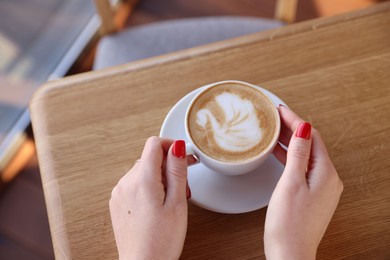 Photo of Woman with cup of aromatic coffee at wooden table in cafe, above view