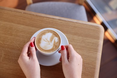 Photo of Woman with cup of aromatic coffee at wooden table in cafe, above view