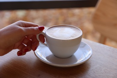 Photo of Woman with cup of aromatic coffee at wooden table in cafe, closeup