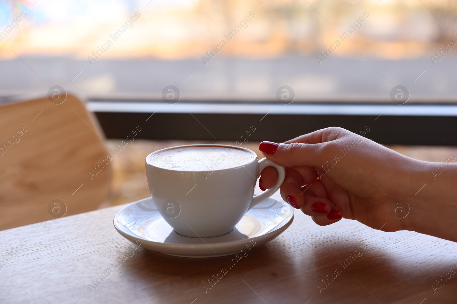 Photo of Woman with cup of aromatic coffee at wooden table in cafe, closeup