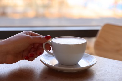 Photo of Woman with cup of aromatic coffee at wooden table in cafe, closeup