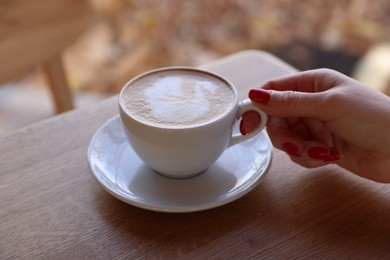 Photo of Woman with cup of aromatic coffee at wooden table in cafe, closeup