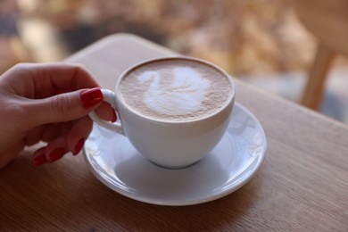 Photo of Woman with cup of aromatic coffee at wooden table in cafe, closeup