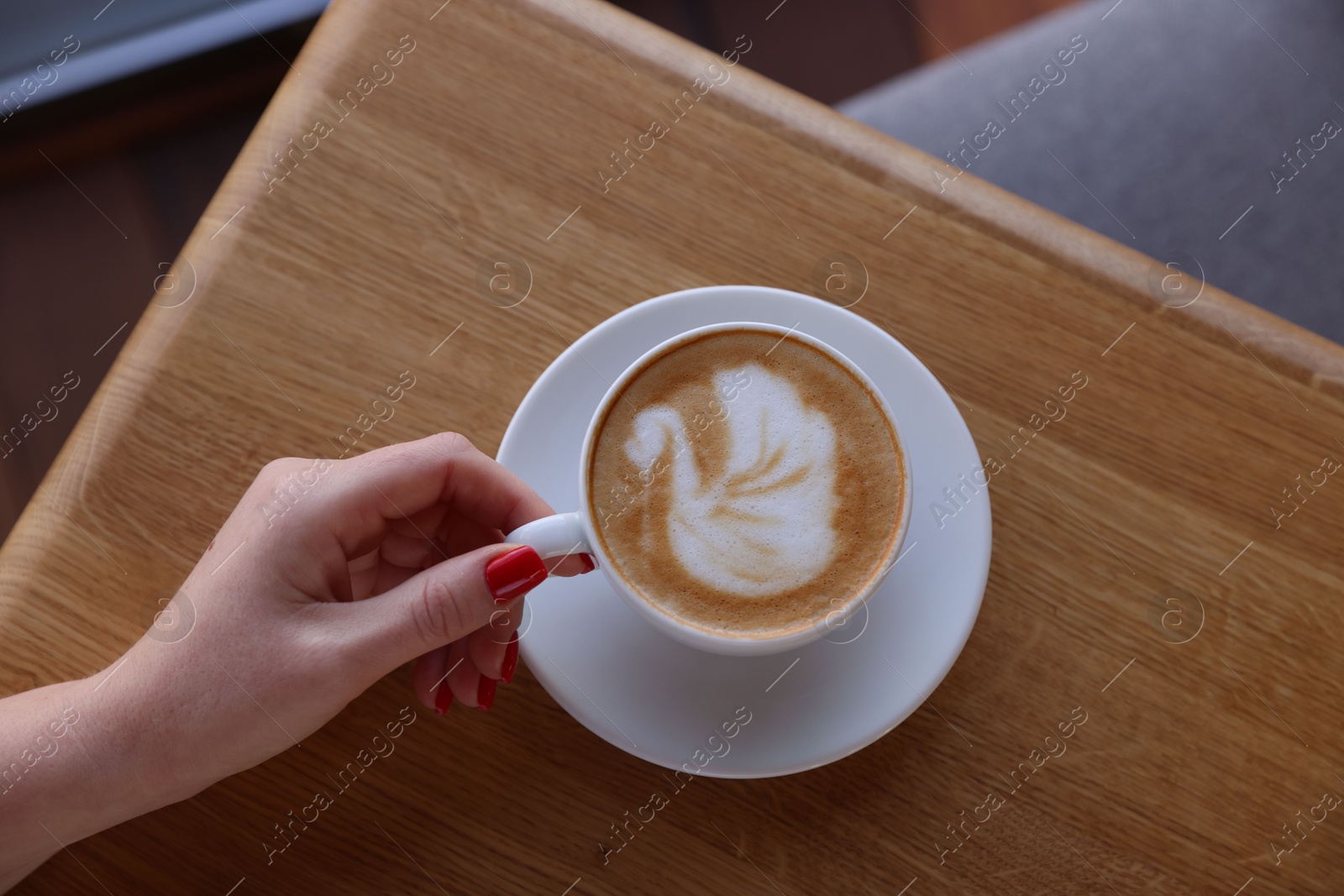 Photo of Woman with cup of aromatic coffee at wooden table in cafe, top view