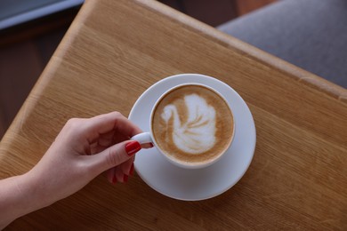 Photo of Woman with cup of aromatic coffee at wooden table in cafe, top view