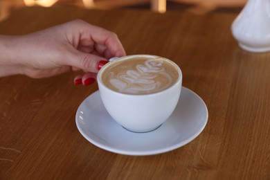 Photo of Woman with cup of aromatic coffee at wooden table in cafe, closeup