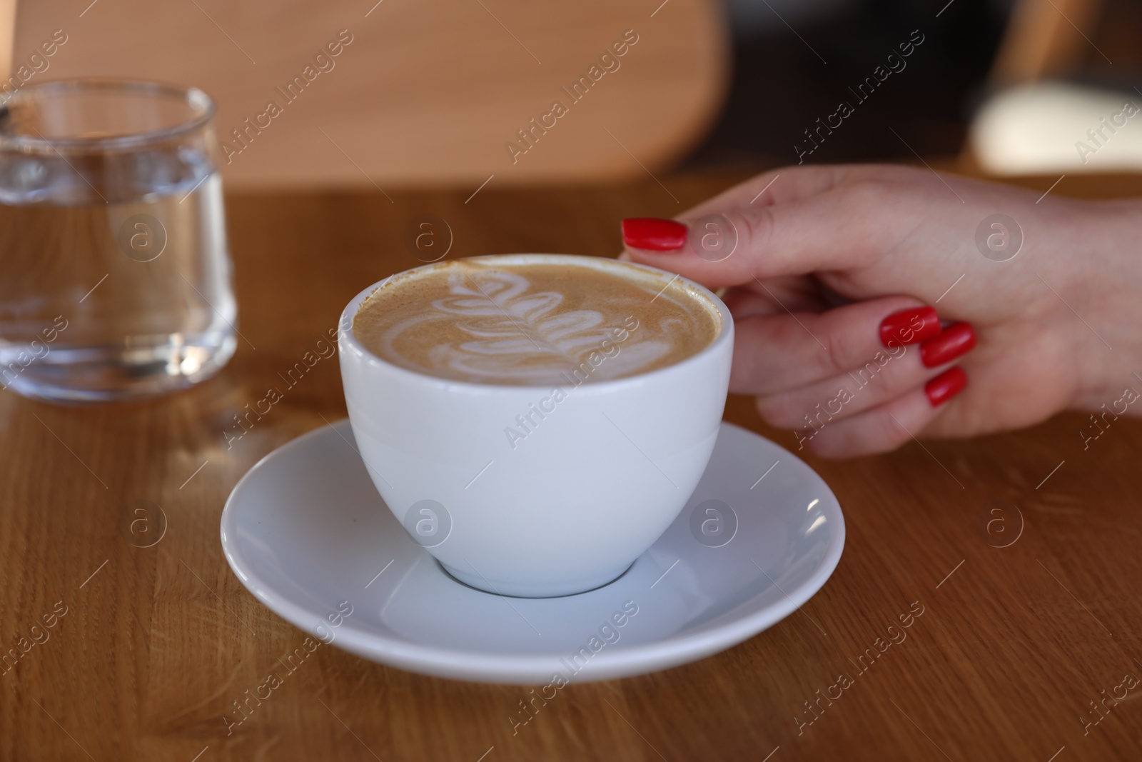 Photo of Woman with cup of aromatic coffee at wooden table in cafe, closeup