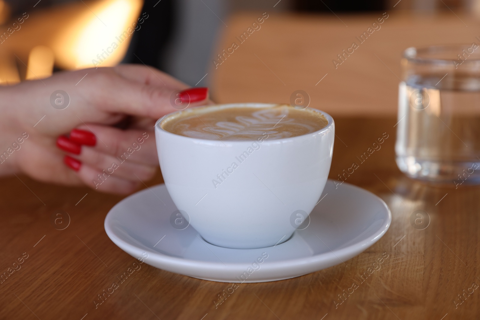 Photo of Woman with cup of aromatic coffee at wooden table in cafe, closeup