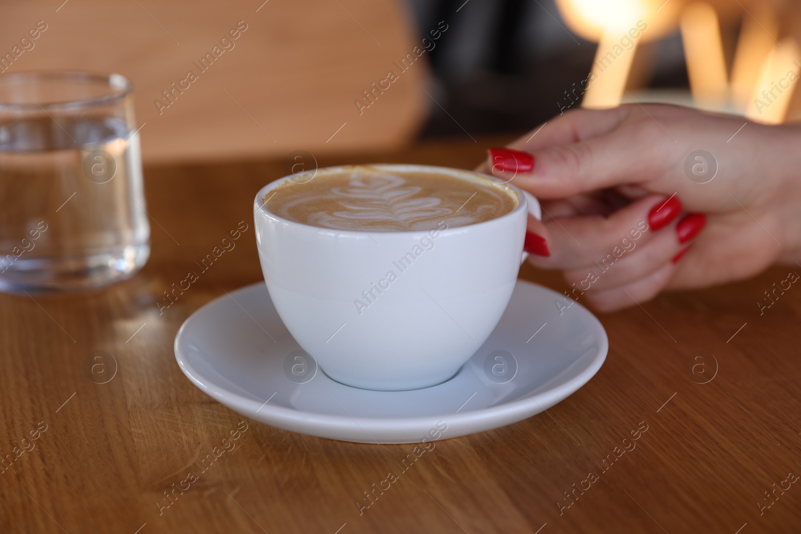 Photo of Woman with cup of aromatic coffee at wooden table in cafe, closeup