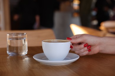 Photo of Woman with cup of aromatic coffee at wooden table in cafe, closeup