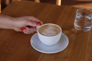 Photo of Woman with cup of aromatic coffee at wooden table in cafe, closeup