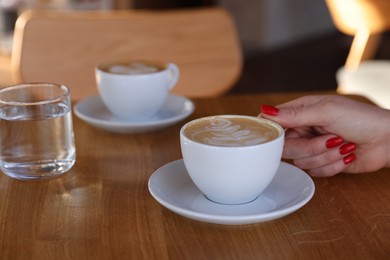 Photo of Woman with cup of aromatic coffee at wooden table in cafe, closeup