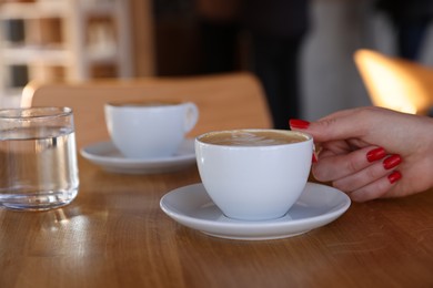 Photo of Woman with cup of aromatic coffee at wooden table in cafe, closeup